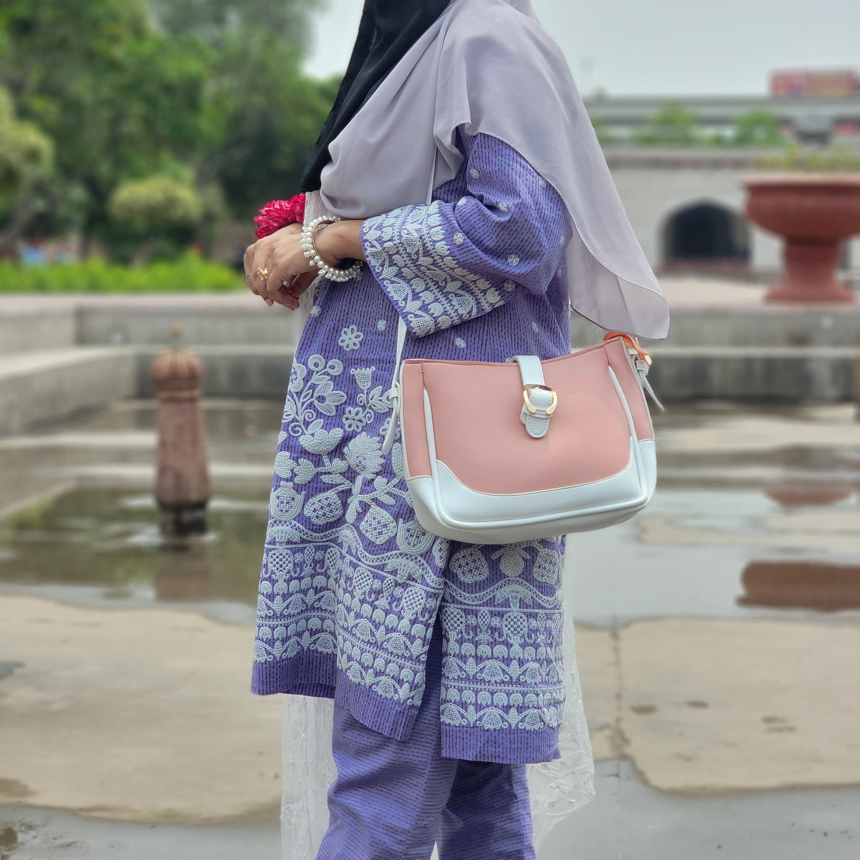 Person wearing a purple and white patterned outfit with a pink and white handbag in an outdoor setting.